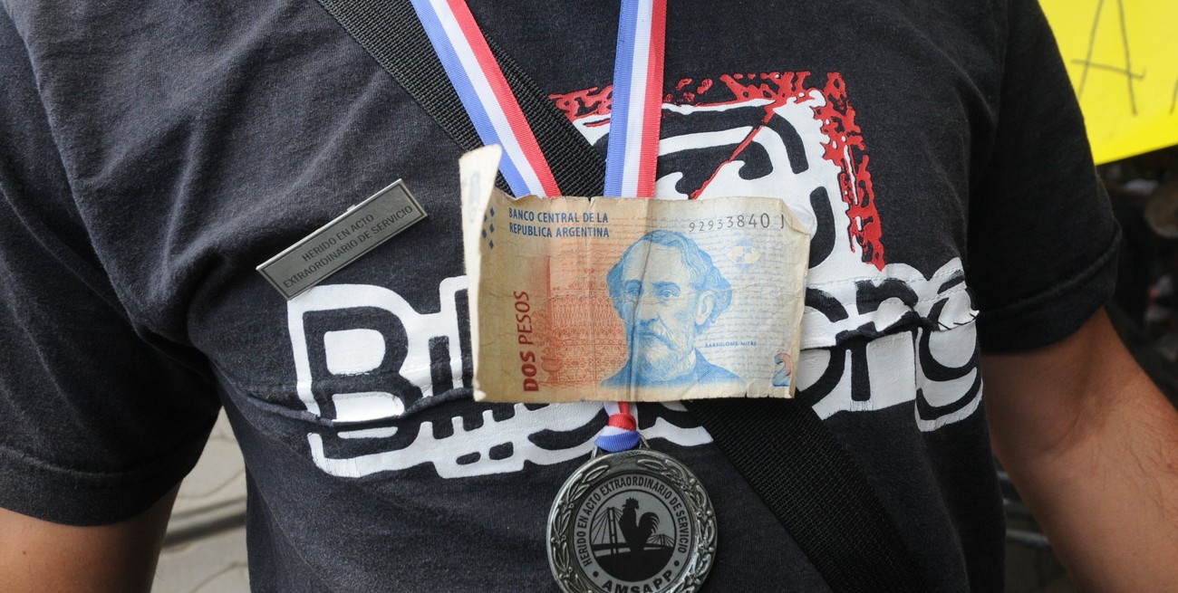 El ya fuera de circulación billete de $2, como símbolo de decadencia del salario, en el pecho de un policía condecorado, herido en un acto de servicio. Foto: Flavio Raina/Archivo