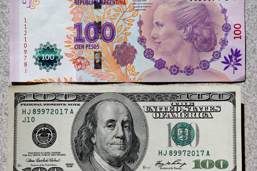 An Argentine 100 pesos bank (above) note, featuring an image of former first lady Eva Peron, is displayed next to a U.S. 100 dollar note in Buenos Aires September 17, 2014. Argentina's peso tumbled 1.87 percent on the black market to hit a record low of 15 per dollar on Wednesday in light trading, traders said. The peso has tanked more than 15 percent since the government defaulted on its debt on July 31, crashing through a succession of historic lows as Argentine businesses and savers seek refuge in dollars.   REUTERS/Enrique Marcarian (ARGENTINA  - Tags:  BUSINESS POLITICS)   billetes 100 pesos y 100 dolares peso dolar devaluacion