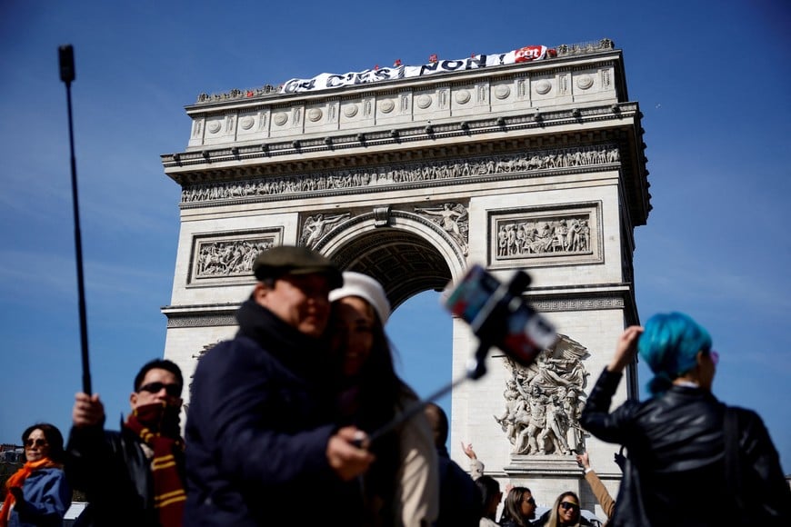 Tourists take pictures as a banner reading "64, it's no" is hung by French CGT labour union members to protest against French government's pension reform, on the top of the Arc de Triomphe in Paris, France, April 5, 2023. REUTERS/Sarah Meyssonnier      TPX IMAGES OF THE DAY
