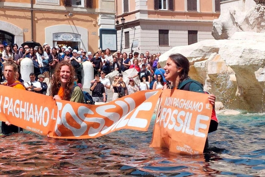 Climate activists hold a banner after pouring vegetable charcoal in the Trevi Fountain water, during a demonstration against fossil fuels, in Rome, Italy May 21, 2023 in this image obtained from social media. Alessandro Penso/MAPS via REUTERS THIS IMAGE HAS BEEN SUPPLIED BY A THIRD PARTY. MANDATORY CREDIT. NO RESALES. NO ARCHIVES.