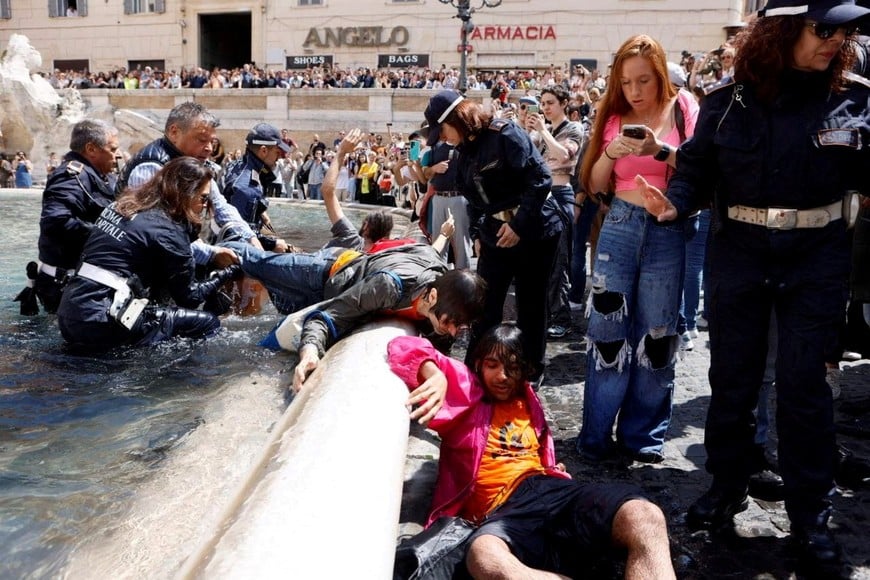 Climate activists are removed from the water by police after pouring vegetable charcoal in the Trevi Fountain, during a demonstration against fossil fuels, in Rome, Italy May 21, 2023 in this image obtained from social media. Alessandro Penso/MAPS via REUTERS THIS IMAGE HAS BEEN SUPPLIED BY A THIRD PARTY. MANDATORY CREDIT. NO RESALES. NO ARCHIVES.
