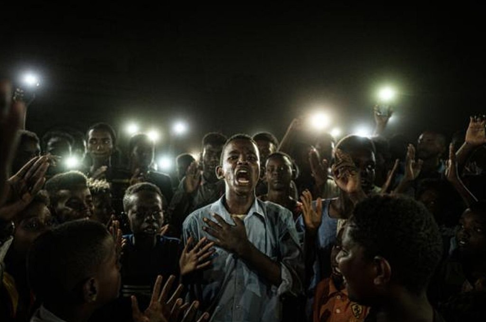 Un joven iluminado por teléfonos móviles mientras recita un poema durante un apagón en Jartum