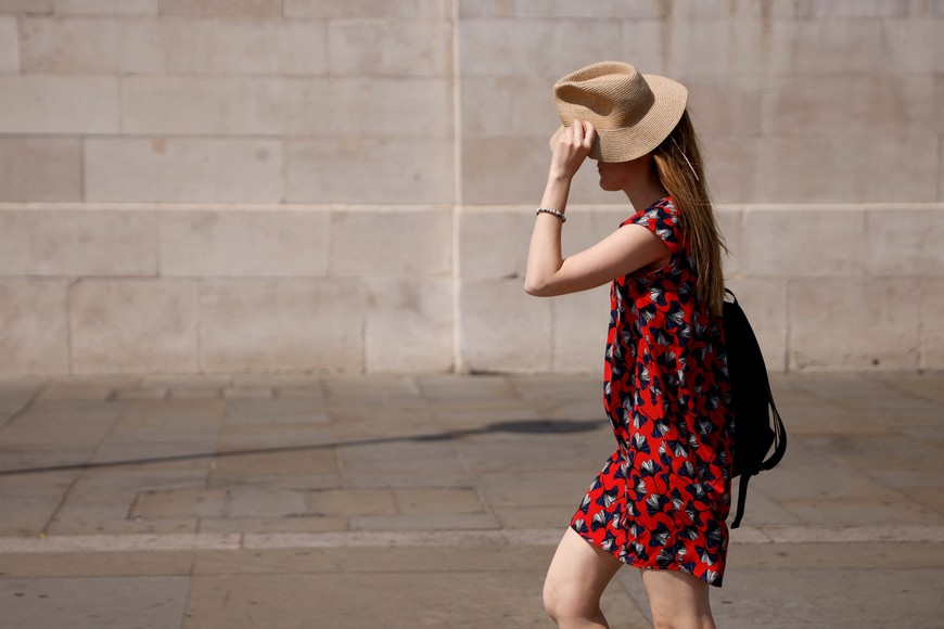 A woman uses a hat to shield her face from the sun in Trafalgar Square during the hot weather in London, Britain, July 18, 2022. REUTERS/John Sibley