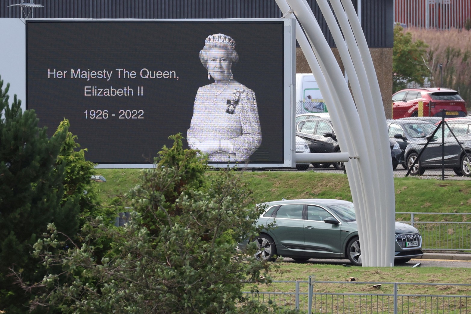 Un automóvil que transporta al rey Carlos y la reina Camila de Gran Bretaña pasa junto a un cartel de la difunta reina Isabel fuera del Aeropuerto Internacional de Aberdeen para volar a Londres, luego del fallecimiento de la reina Isabel de Gran Bretaña, en Aberdeen, Gran Bretaña. Reuters/Phil Noble