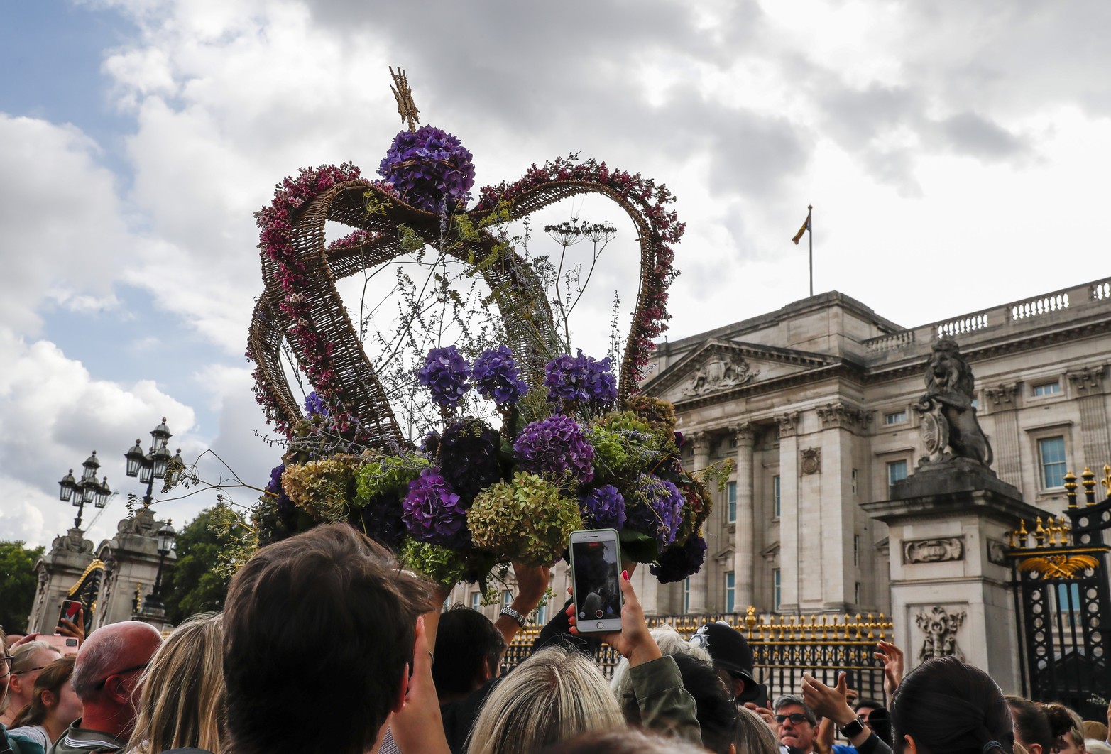 Ppersonas trasladando un arreglo floral en forma de corona gigante como tributo a la fallecida reina Isabel II de Reino Unido, en Londres. Xinhua/Han Yan