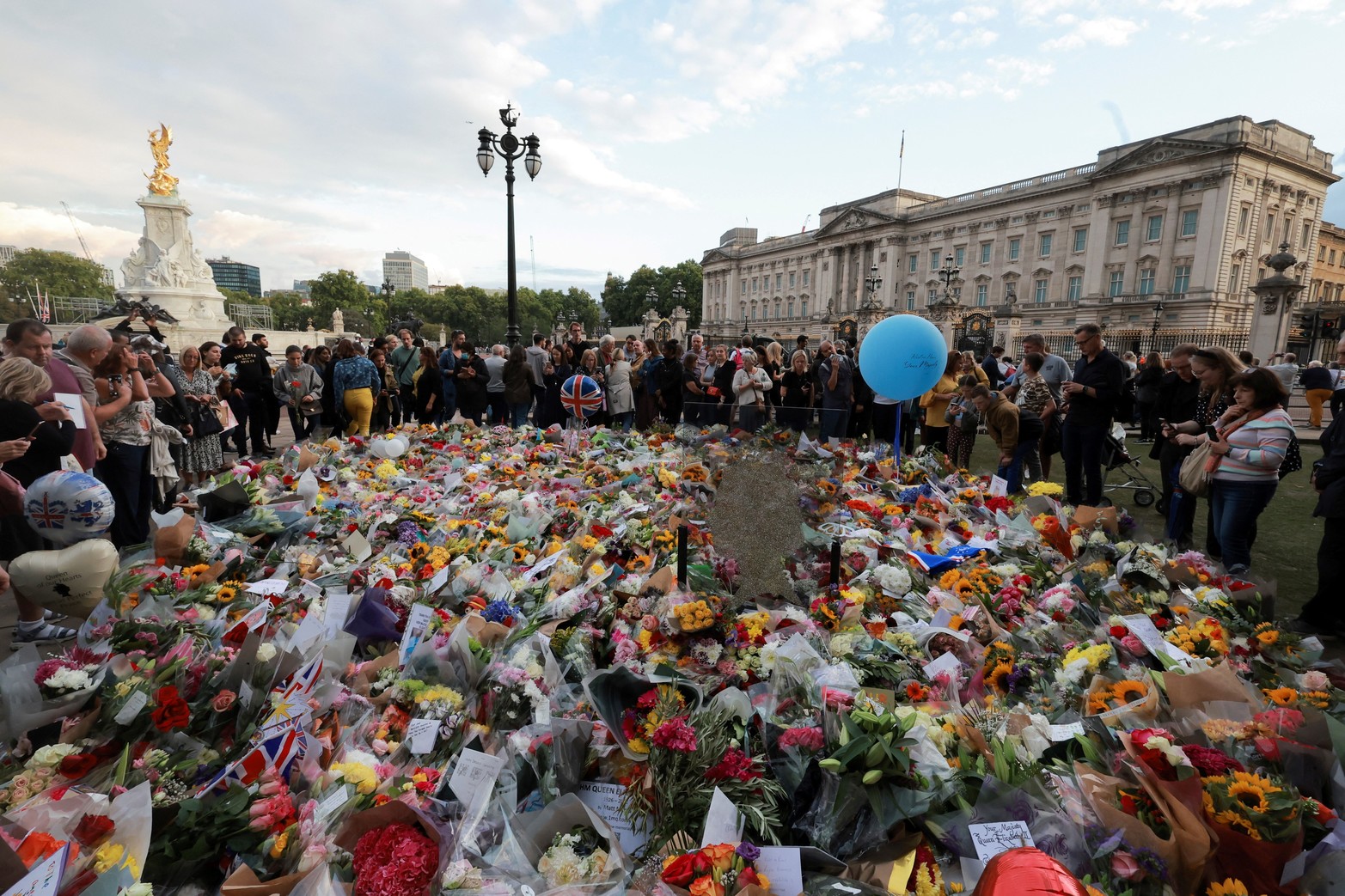 La gente se reúne alrededor de los tributos florales colocados fuera del Palacio de Buckingham, tras el fallecimiento de la Reina Isabel de Gran Bretaña. Reuters/Marko Djurica
