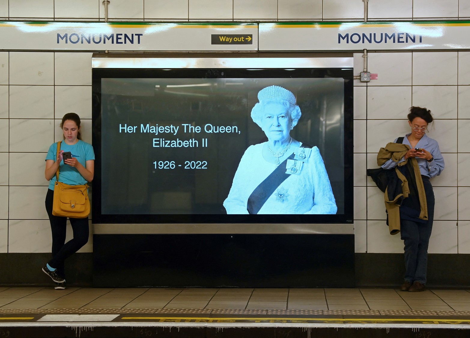 Los pasajeros del tren subterráneo de Londres esperan en una plataforma junto a una imagen de cartelera de la reina Isabel de Gran Bretaña. Reuters /Toby Melville