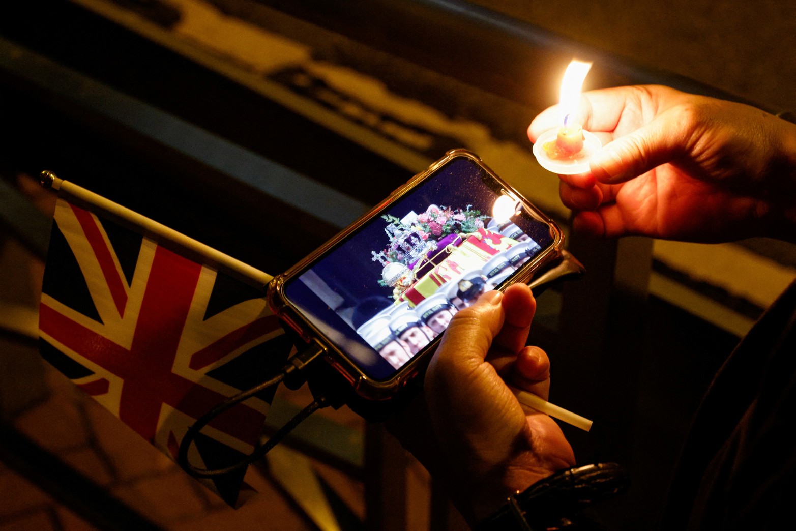 Un hombre ve una retransmisión en vivo del funeral de la Reina Isabel de Gran Bretaña con una vela y una bandera Union Jack, fuera del Consulado General Británico, en Hong Kong, China.  Reuters/Tyrone Siu