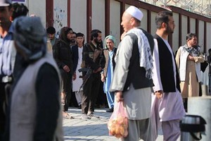 Combatientes talibanes hacen guardia mientras la gente se reúne para buscar a sus familiares fuera de un hospital. Crédito: AFP.