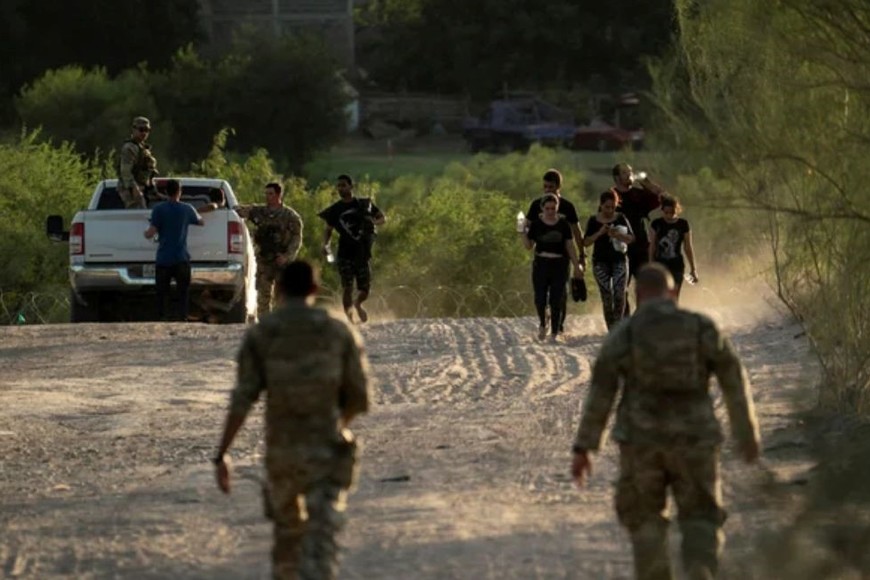 Migrantes que buscan asilo caminan mientras son escoltados por oficiales de la Guardia Nacional de EEUU.