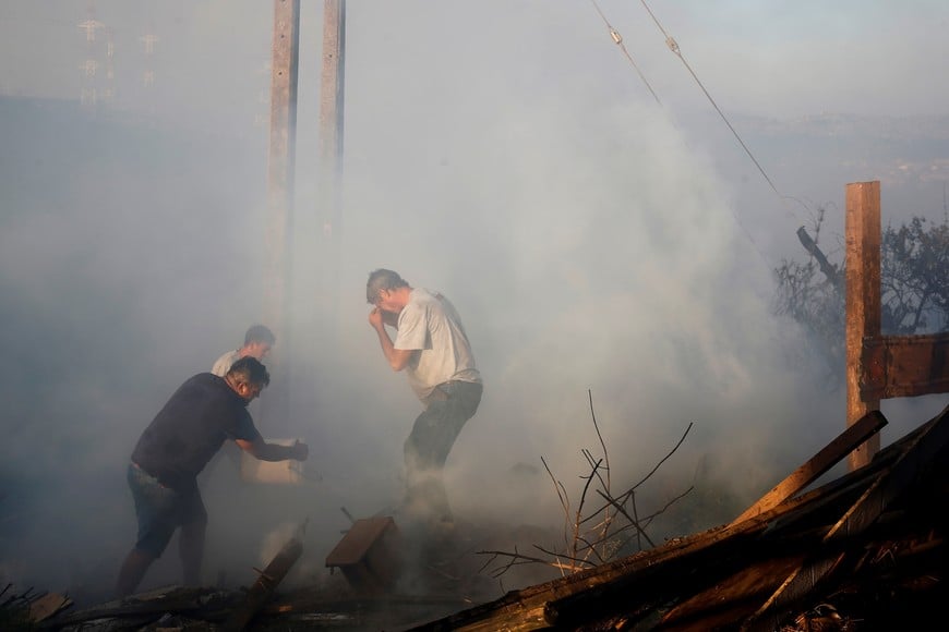 A man pours water over the remains of a burned house during a wildfire in Vina del Mar, Chile  December 22, 2022. REUTERS/Rodrigo Garrido