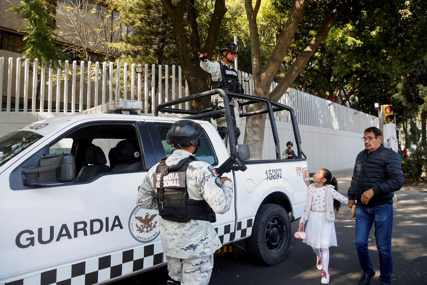 A man and a girl pass by as members of the National Guard keep watch following the detention of Mexican drug gang leader Ovidio Guzman, a son of incarcerated kingpin Joaquin "El Chapo" Guzman, who has been arrested by Mexican authorities, outside the building of the Attorney General's Office for Special Investigations on Organized Crime (FEMDO), in Mexico City, Mexico January 5, 2023. REUTERS/Raquel Cunha