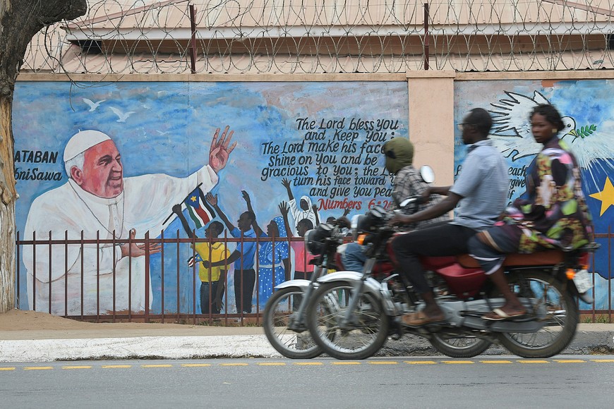 Motociclistas pasan frente a un mural que representa al Papa Francisco mientras continúan los preparativos antes de su visita en Juba.
