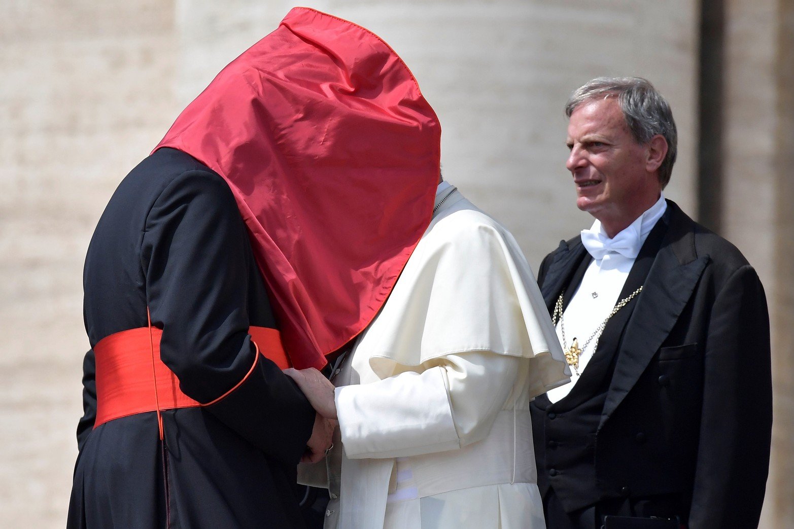Una ráfaga de viento levanta la mantilla de un cardenal no identificado mientras estrecha la mano del Papa Francisco al final de una audiencia como parte del Año Jubilar de la Misericordia el 30 de abril de 2016 en la plaza de San Pedro en el Vaticano. 