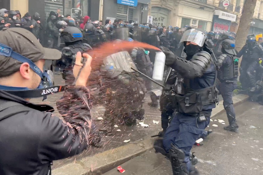 A man records the scene of a riot police officer on fire, to the left, as another officer sprays him and the crowd with an irritant, during May Day protests in Paris, France May 1, 2023 in this still image from social media video. Timothee Forget via REUTERS ATTENTION EDITORS - THIS IMAGE HAS BEEN SUPPLIED BY A THIRD PARTY. MANDATORY CREDIT. NO RESALES. NO ARCHIVES. FRANCE OUT. NO COMMERCIAL OR EDITORIAL SALES IN FRANCE