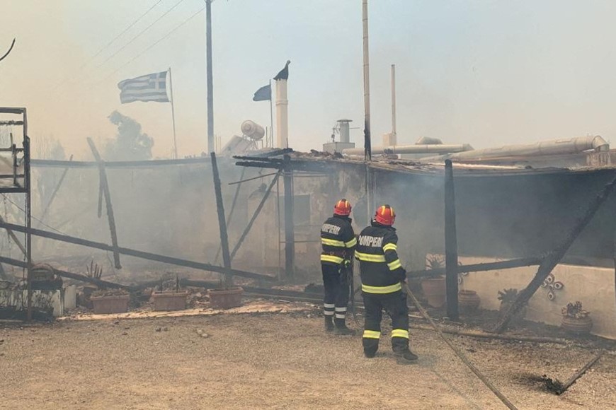 Romanian firefighters try to extinguish a fire at a burning building, as a wildfire burns on the island of Rhodes, Greece, July 24, 2023. Romanian Government's Department for Emergencies/Handout via REUTERS THIS IMAGE HAS BEEN SUPPLIED BY A THIRD PARTY. MANDATORY CREDIT. NO RESALES. NO ARCHIVES. BEST QUALITY AVAILABLE.