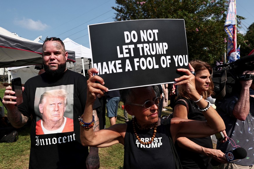 An anti-Trump demonstrator holds a banner next to a supporter of former U.S. President Donald Trump near the entrance of the Fulton County Jail, as Donald Trump is expected to turn himself in to be processed after his Georgia indictment, in Atlanta, Georgia, U.S., August 24, 2023. REUTERS/Dustin Chambers
