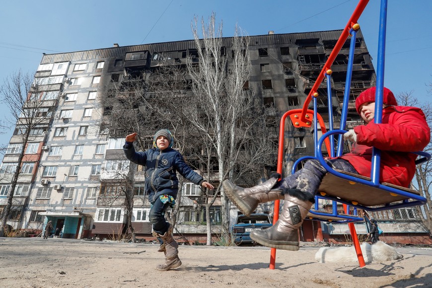 Children play in front of a building damaged in fighting during Ukraine-Russia conflict, in the besieged southern port of Mariupol, Ukraine March 23, 2022.  REUTERS/Alexander Ermochenko