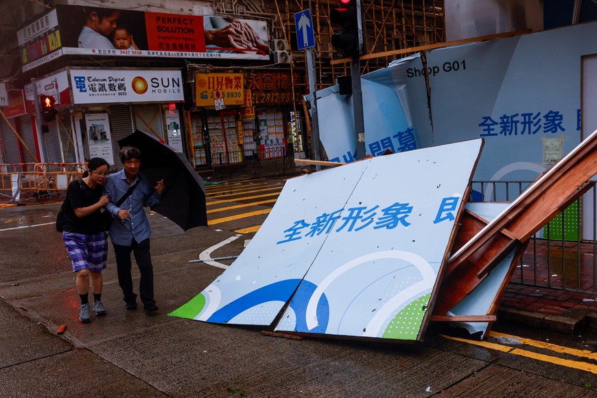 People brave strong winds near a fallen billboard following Super Typhoon Saola, in Hong Kong, China September 2, 2023. REUTERS/Tyrone Siu