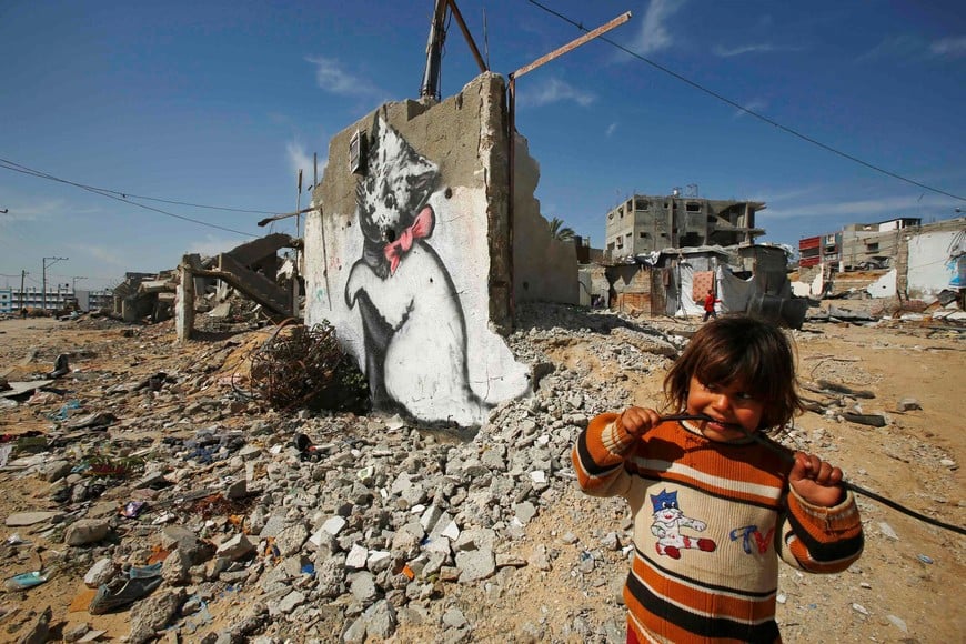 A Palestinian girl looks on as a mural of a playful-looking kitten, presumably painted by British street artist Banksy, is seen on the remains of a house that witnesses said was destroyed by Israeli shelling during a 50-day war last summer, in Biet Hanoun town in the northern Gaza Strip February 26, 2015. The anonymous but eminent British street artist known as Banksy has posted a mini-documentary on his banksy.co.uk site showing squalid conditions in Gaza six months after the end of the war between the enclave's Islamist Hamas rulers and Israel. REUTERS/Suhaib Salem (GAZA - Tags: POLITICS CIVIL UNREST SOCIETY TPX IMAGES OF THE DAY) franja de gaza  franja de gaza obra mural artista Banksy arte murales muralismo arte callejero