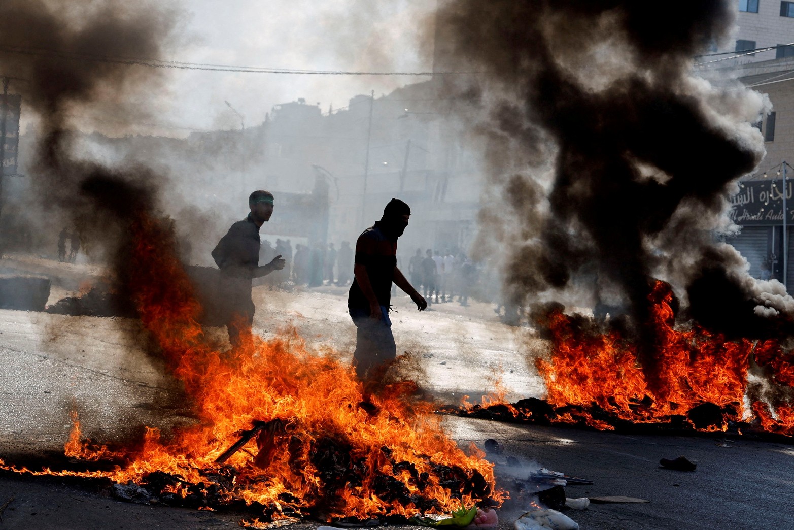 La gente camina junto a los incendios mientras los palestinos participan en una protesta tras los ataques israelíes en Gaza, en Naplusa, en la Cisjordania ocupada por Israel.