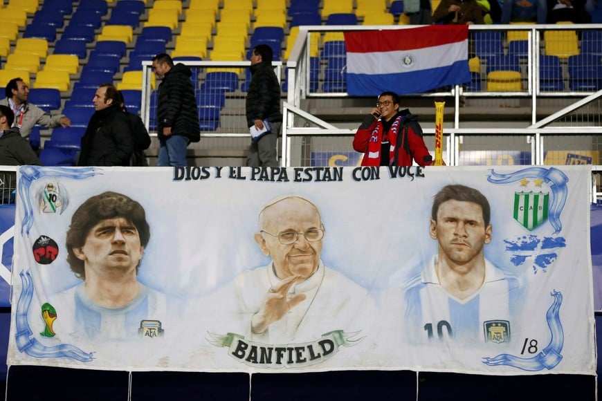 A Chile fan stands behind a banner depicting (L-R) retired Argentina soccer player Diego Maradona, Pope Francis and Argentina's Lionel Messi as he awaits the start of the Copa America 2015 semi-final soccer match between Argentina and Paraguay at Estadio Municipal Alcaldesa Ester Roa Rebolledo in Concepcion, Chile, June 30, 2015. REUTERS/Andres Stapff chile  futbol campeonato copa america 2015 partido seleccion argentina vs paraguay color hinchas hinchada hinchadas