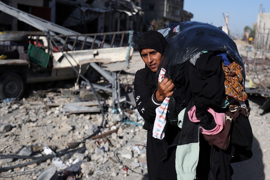 A displaced Palestinian woman carries a bag of clothes as she returns to her home walking next to houses destroyed in an Israeli strike during the conflict, amid the temporary truce between Hamas and Israel, in Khan Younis in the southern Gaza Strip November 24, 2023. REUTERS/Ibraheem Abu Mustafa