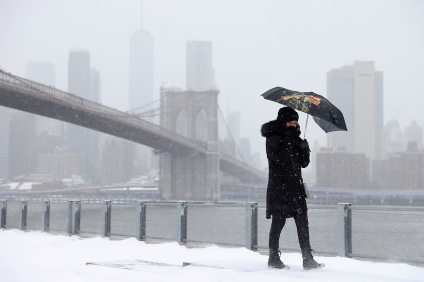 A person walks in front of the Brooklyn Bridge in the snow during a Nor'easter storm in Brooklyn, New York City, U.S., January 29, 2022. REUTERS/Andrew Kelly