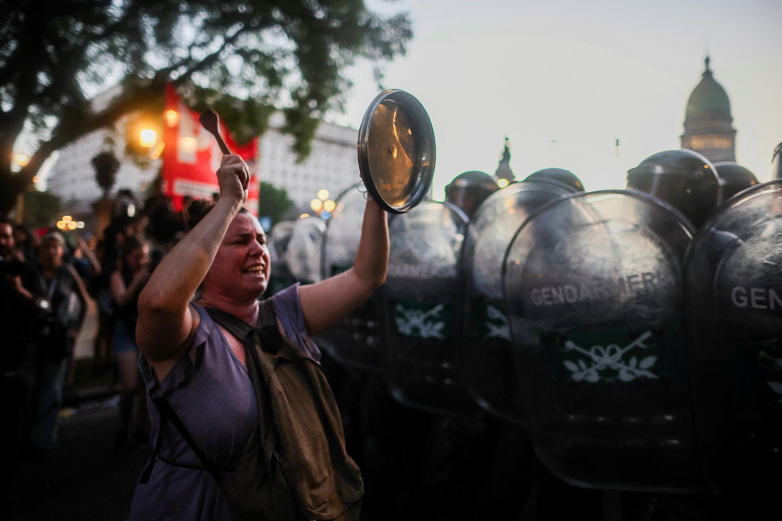 Una mujer golpea una tapa mientras agentes del orden hacen guardia mientras los manifestantes protestan frente al Congreso Nacional el día del debate sobre el proyecto de reforma económica del presidente argentino Javier Milei, conocido como el "proyecto de ley ómnibus". 