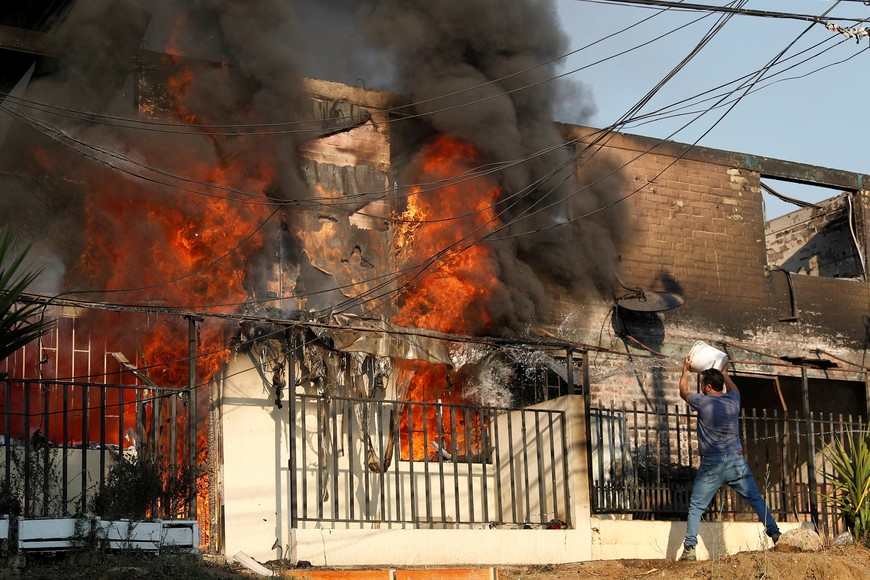 A man tries to extinguish a fire burning a house during the spread of wildfires in Vina del Mar, Chile February 3, 2024. REUTERS/Rodrigo Garrido