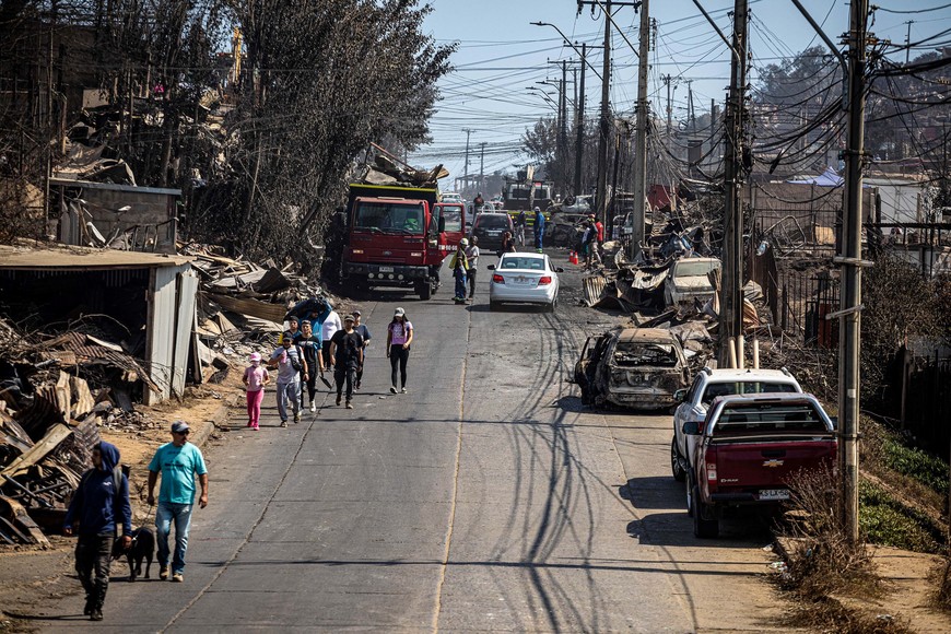 (240205) -- VIÑA DEL MAR, 5 febrero, 2024 (Xinhua) -- Personas caminan frente a casas y restos de automóviles destruidos por un incendio forestal, en Viña del Mar, Chile, el 5 de febrero de 2024. El número de las personas fallecidas por los incendios forestales que afectan a la región chilena de Valparaíso, en la zona central del país sudamericano, aumentó a 122, informó el lunes el Gobierno de Chile. (Xinhua/Str) (jv) (rtg) (ah) (vf)