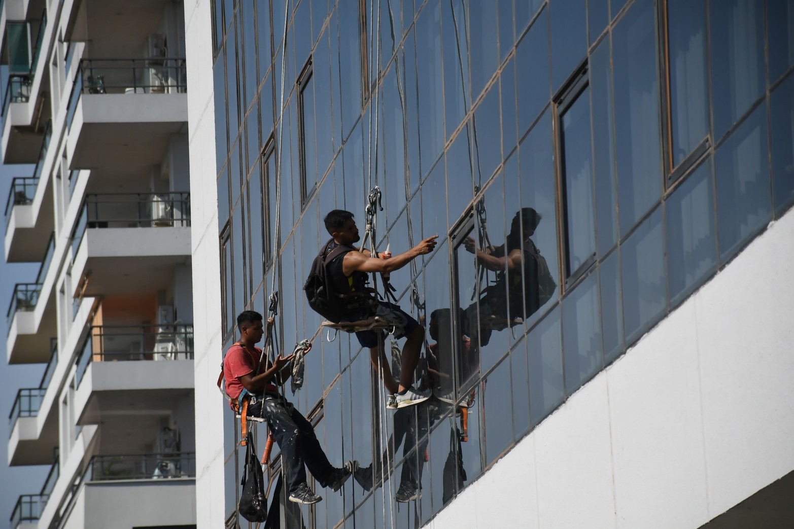 Sellando. Obreros trabajan sobre una pared de vidrios en la construcción de un edificio.