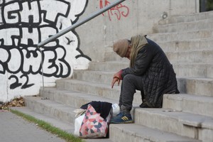 Una persona indigente, abatida, sentada en la escalera que da a un parque público. La pobreza y la desocupación golpean duro a los sectores socialmente vulnerables. Crédito: Mauricio Garín