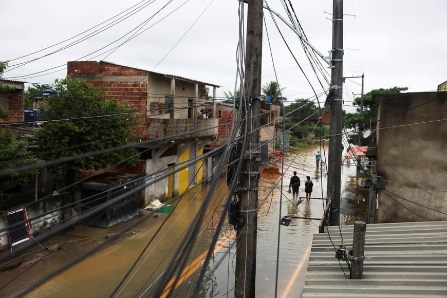 People walk on a flooded street after heavy rains in Duque de Caxias, Rio de Janeiro state, Brazil, March 24, 2024. REUTERS/Pilar Olivares