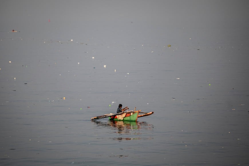 A woman fishes from a boat while trash floats in the waters of Baseco Beach on World Oceans Day, in Manila, Philippines, June 8, 2023. REUTERS/Eloisa Lopez     TPX IMAGES OF THE DAY