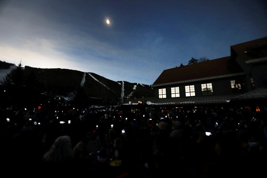 The sky darkens as people take photos with their phones of the total solar eclipse at Sugarbush ski resort in Warren, Vermont, U.S. April 8, 2024.  REUTERS/Lauren Owens Lambert