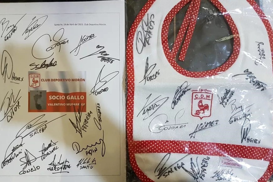El carné y un babero (regalo de hinchas de Morón) autografiados por el plantel del Gallo.