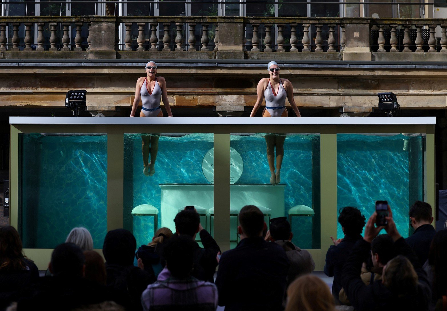 La gente observa cómo los ex nadadores artísticos olímpicos británicos Asha George y Katie Clark de Aquabatix actúan en un gran tanque de agua para marcar 100 días antes de que comiencen los Juegos Olímpicos de París 2024, en Covent Garden en Londres, Gran Bretaña.