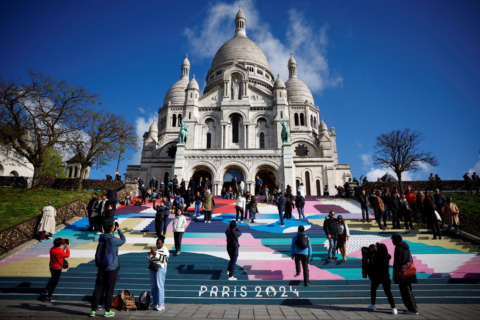 Los turistas se encuentran en las escaleras de la Basílica del Sacre-Coeur pintadas con el diseño de los Juegos Olímpicos y Paralímpicos de París 2024 en la Butte Montmartre en París, Francia