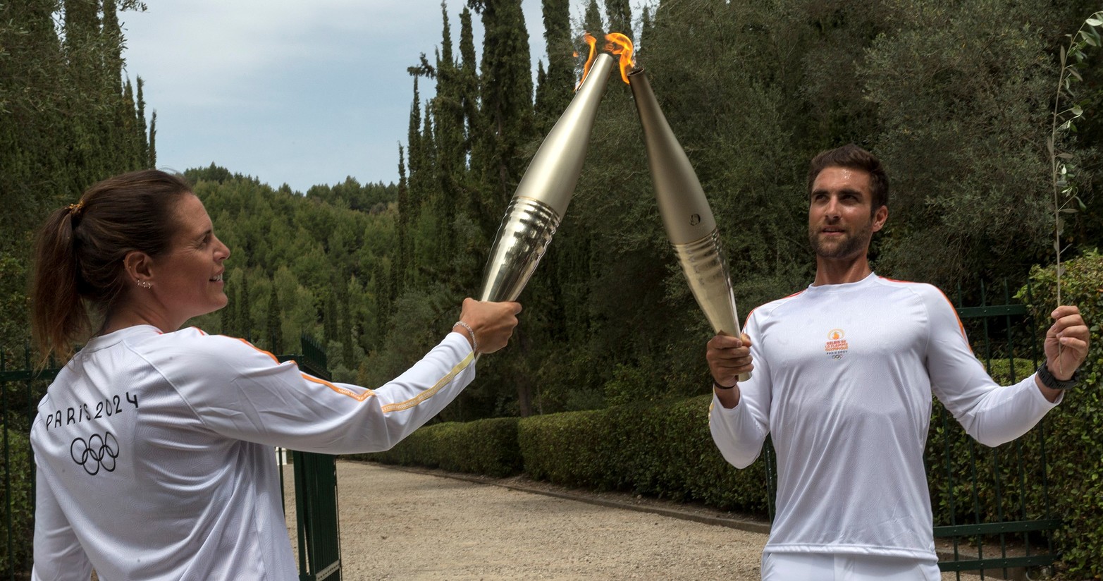  El primer portador de la antorcha, el campeón olímpico griego de remo, Stefanos Ntouskos (d), enciende la antorcha de la segunda portadora de la antorcha, la campeona olímpica francesa de natación, Laure Manaudou, durante el relevo de la antorcha después de la ceremonia de encendido de la llama olímpica de los Juegos Olímpicos de París 2024, en la Antigua Olimpia, Grecia