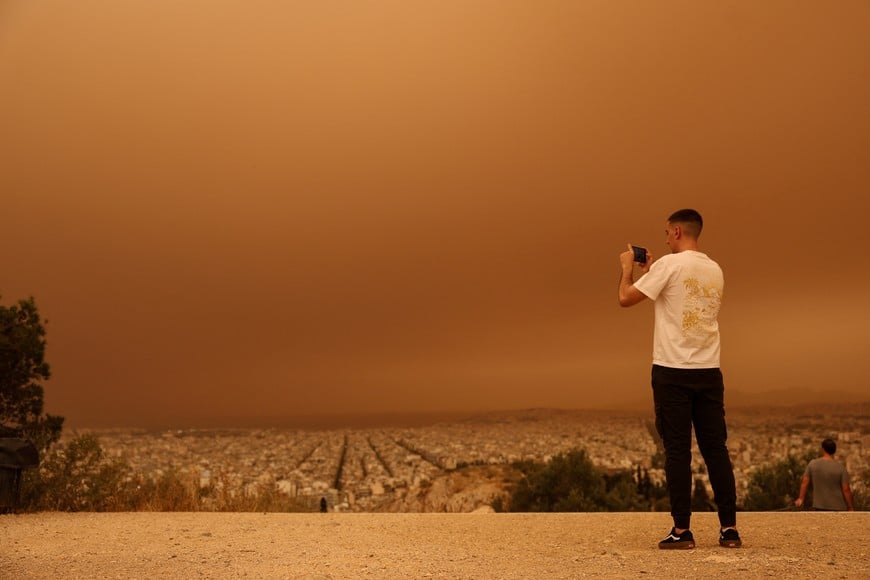 A man takes pictures as African dust from the desert of Sahara covers the city of Athens, Greece, April 23, 2024. REUTERS/Louisa Gouliamaki