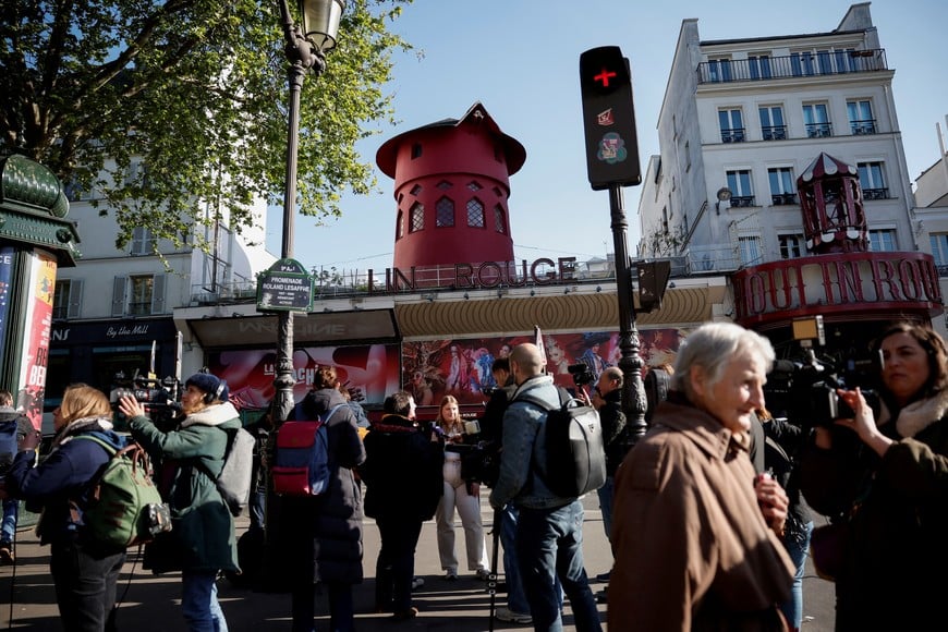 People interact with media personnel in front of the Moulin Rouge, Paris' most famous cabaret club, after the sails of the landmark red windmill on its top fell off during the night in Paris, France, April 25, 2024. REUTERS/Benoit Tessier