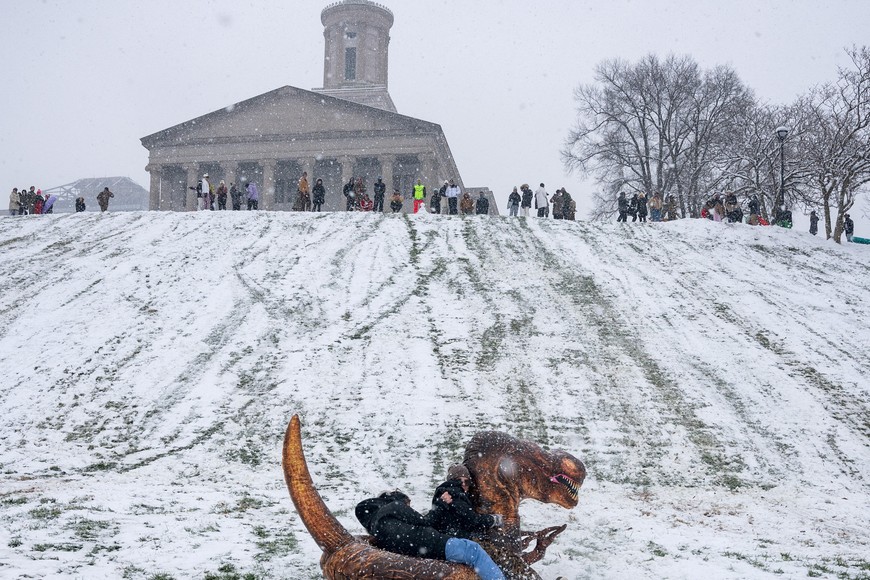 People sled on an inflatable dinosaur on Capitol Hill as Winter Storm Cora makes its way through the Southern United States, in Nashville, Tennessee, U.S. January 10, 2025.  REUTERS/Seth Herald     TPX IMAGES OF THE DAY