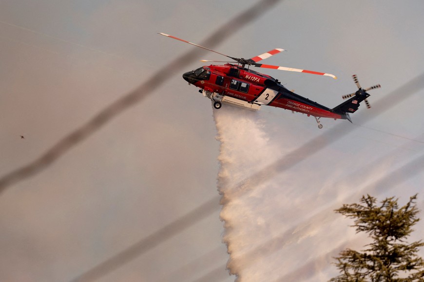 A helicopter drops water on the Palisades Fire, one of several simultaneous blazes that have ripped across Los Angeles County, along Mandeville Canyon, in the Encino neighborhood of Los Angeles, California, U.S., January 11, 2025. REUTERS/Daniel Dreifuss