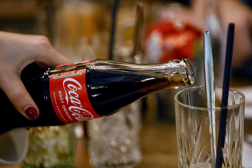 A waitress holds a bottle of Coca-Cola to serve a customer in a bar in Paris, France, January 28, 2025. REUTERS/Abdul Saboor