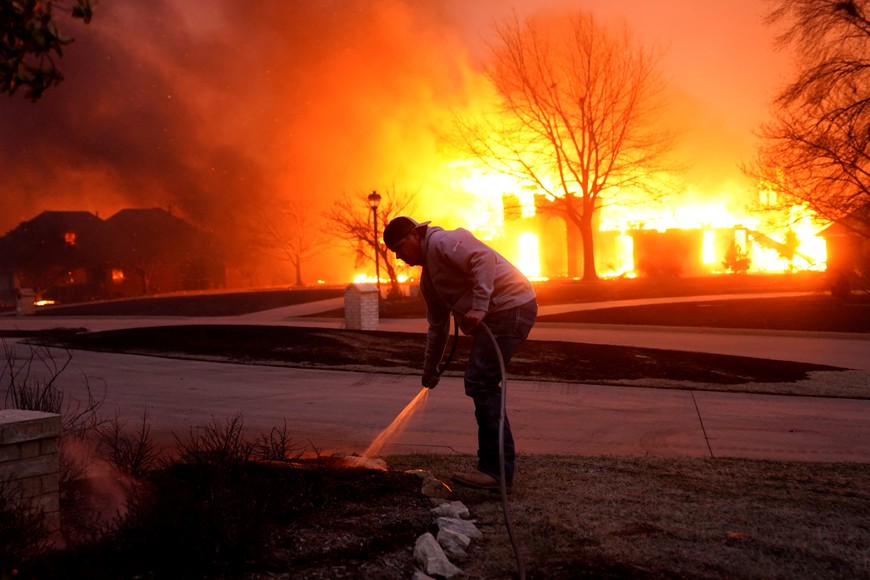 Cody McIntire sprays water on a fire burning in a yard in front of his friend's house during a wildfire outbreak in Stillwater, Oklahoma, U.S., March 14, 2025.  REUTERS/Nick Oxford