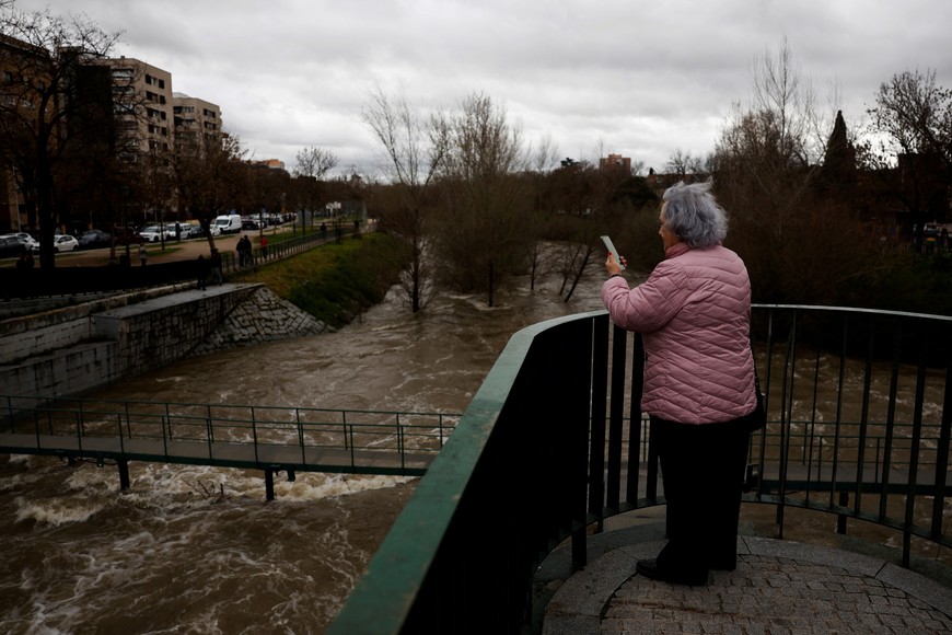 A woman uses a mobile phone to record the unusually high levels of water of the Manzanares river after weeks of rain in Madrid, Spain, March 21, 2025. REUTERS/Susana Vera