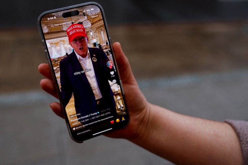 FILE PHOTO: A woman poses with her smartphone displaying the @realdonaldtrump TikTok page, in Washington, U.S. January 19, 2025. REUTERS/Shannon Stapleton/File Photo