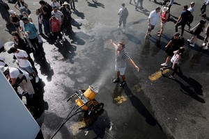 A man cools off under a water sprayer as visitors queue to refill their bottles with water on a warm and sunny day at the 55th International Paris Airshow at Le Bourget Airport near Paris, France, June 20, 2025. REUTERS/Benoit Tessier
