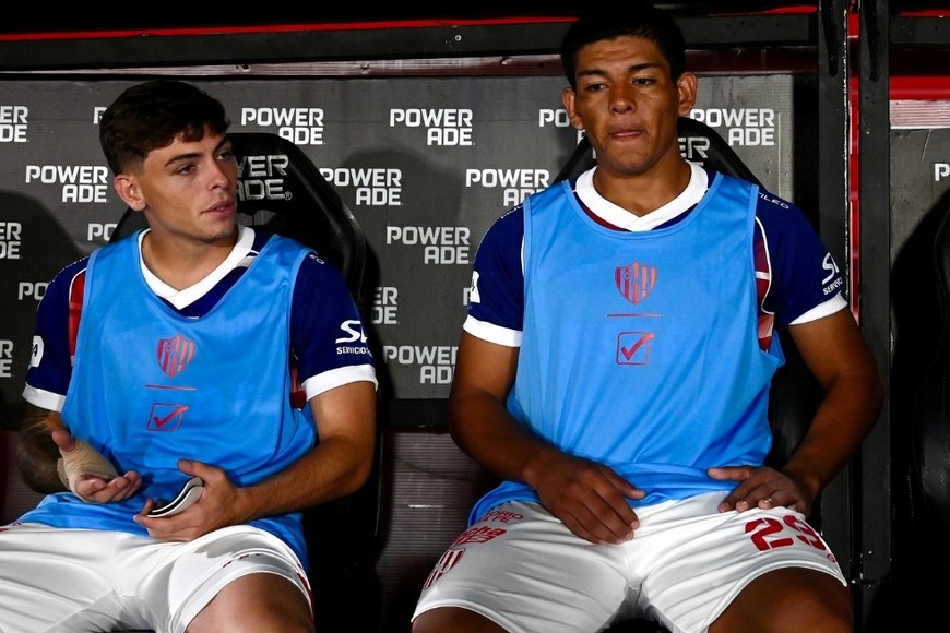 Jerónimo Dómina al lado de Diego Armando Díaz, sentaditos en el banco de suplentes del Tate. Foto: Juan Foglia.